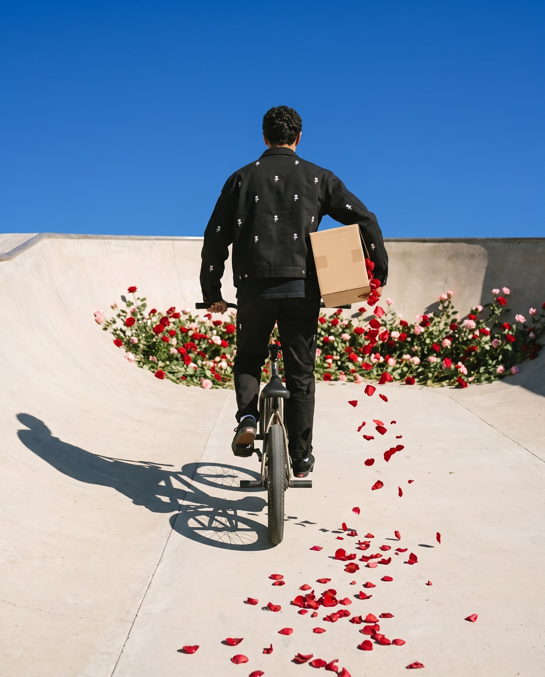 Riding off across the concrete with the sealed box under one arm, petals trailing behind